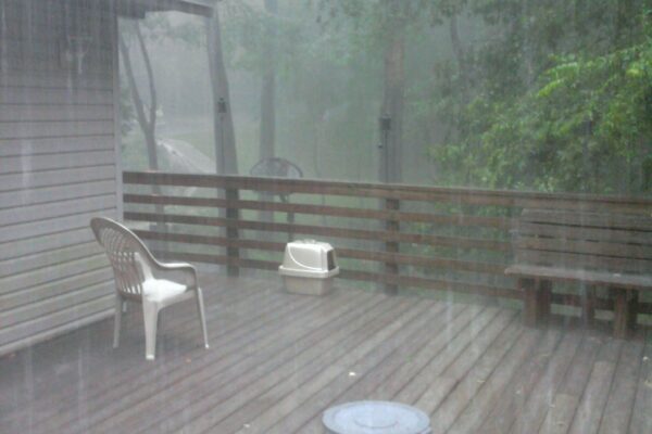Image shows a deck in heavy rain. Beyond the deck is a waterfall caused by stormwater runoff