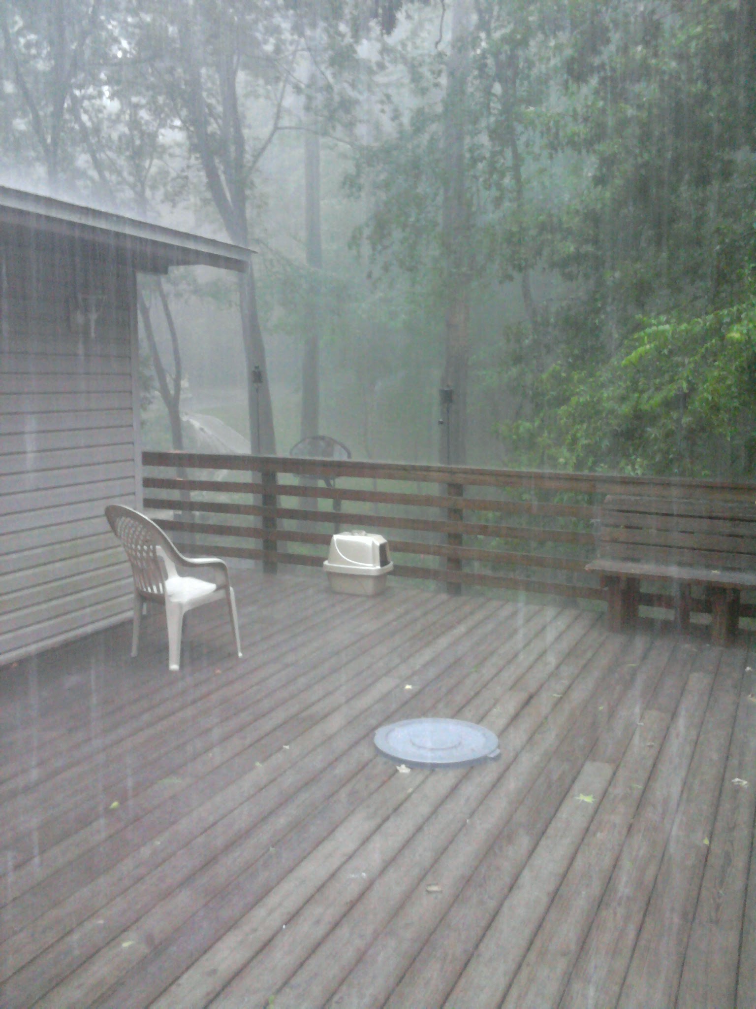 Image shows a deck in heavy rain. Beyond the deck is a waterfall caused by stormwater runoff